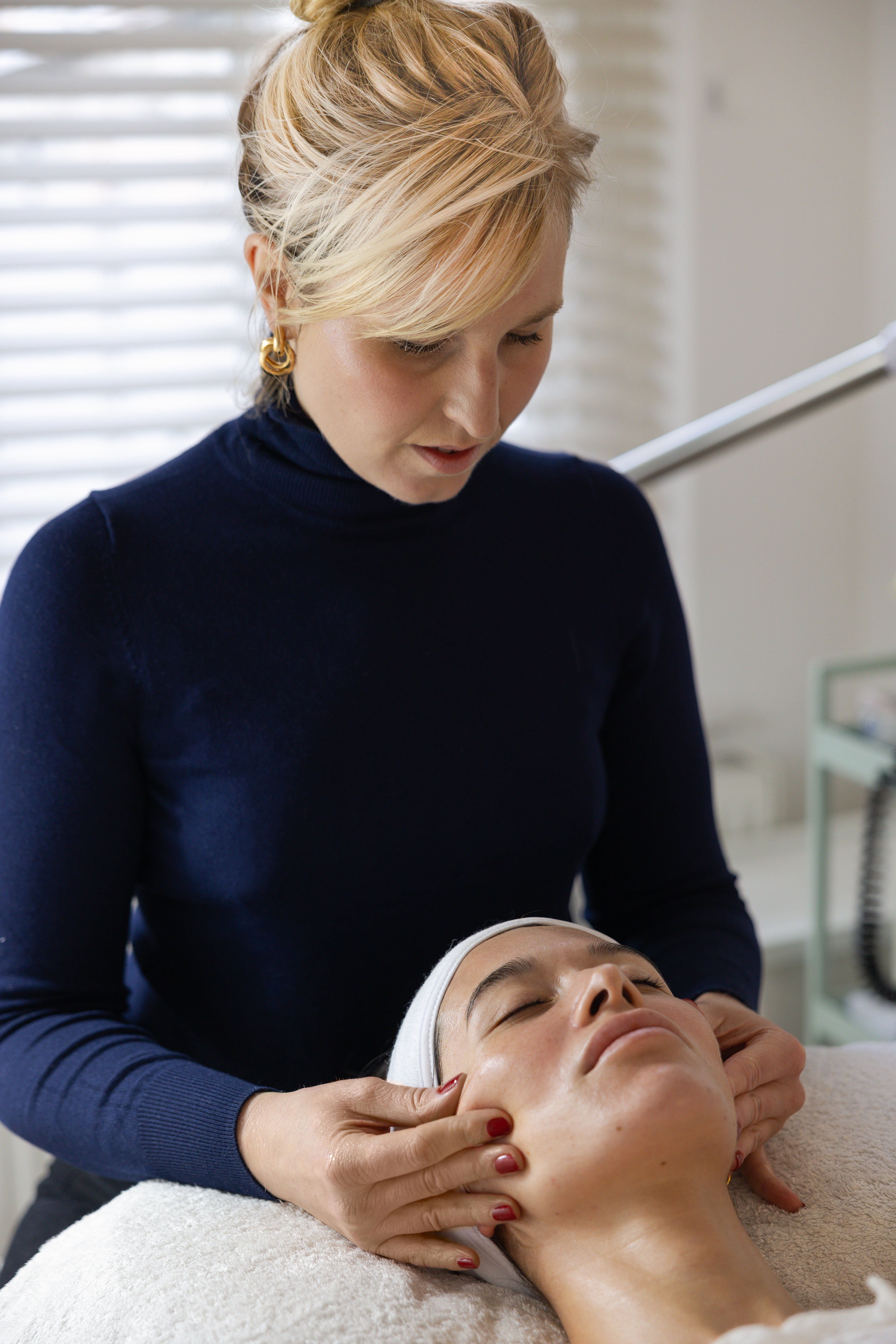 Woman receiving a facial massage from Rhian Truman with children of earth skincare products in a clinical setting.